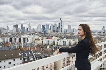 Nachdenkliche Geschäftsfrau mit Blick auf das Stadtbild auf der Terrasse eines Gebäudes - AKLF00189