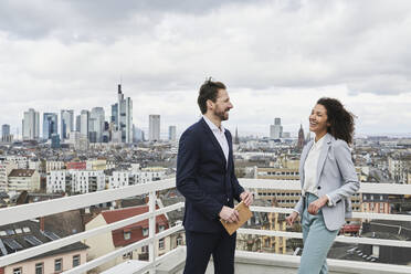 Lächelnde Partner, die sich auf der Terrasse eines Gebäudes unterhalten - AKLF00195