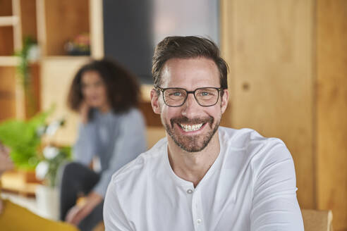 Cheerful mature entrepreneur with female colleague in background at creative office - AKLF00216