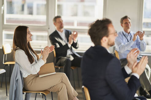 Businesswoman clapping hands with colleagues in education conference centre - AKLF00244