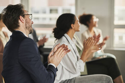 Businessman clapping hands with colleagues in conference event - AKLF00259