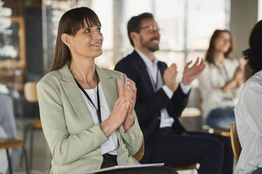 Businesswoman clapping hands with colleagues in conference centre - AKLF00260