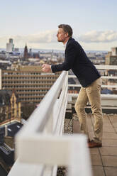 Thoughtful businessman leaning on terrace railing - AKLF00277