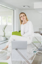 Businesswoman with hand on chin sitting in front of laptop at office - MCVF00871