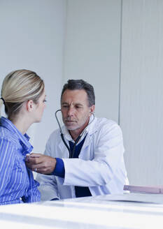 Männlicher Arzt, der eine Patientin mit Stethoskop im Krankenhaus untersucht - AJOF01320
