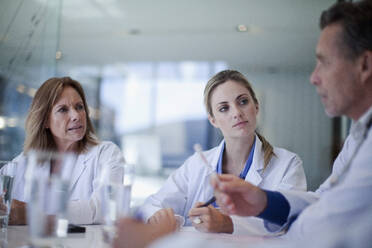 Weibliche Ärzte schauen auf einen männlichen Mitarbeiter des Gesundheitswesens, der während einer Besprechung im Krankenhaus erklärt - AJOF01327