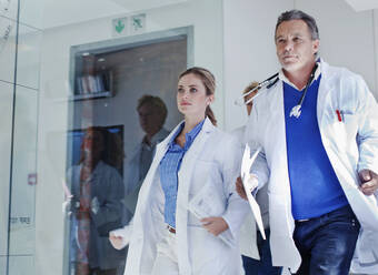 Weibliche und männliche Ärzte, die während eines Notfalls im Krankenhaus auf dem Korridor laufen - AJOF01334