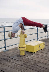 Mann balanciert auf Hydrant am Geländer des Santa Monica Piers - AJOF01348