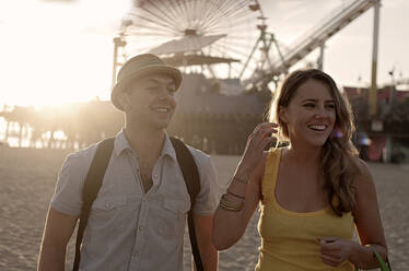 Lächelndes Paar schaut weg, während es seinen Urlaub am Pier von Santa Monica genießt - AJOF01351