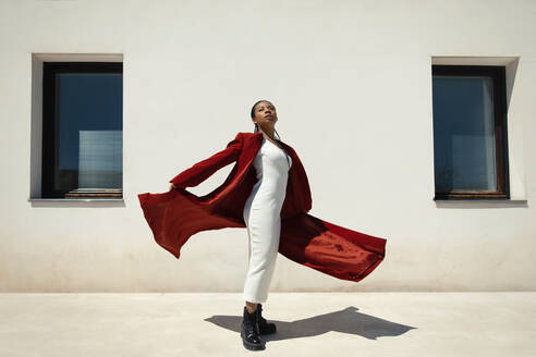 Young woman wearing overcoat standing in front of wall - TCEF01844