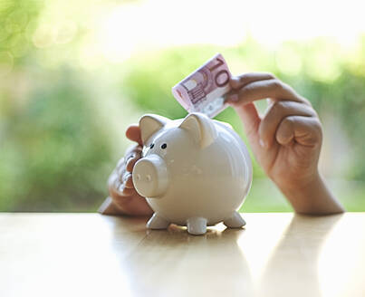 Boy inserting 10 Euro note in piggy bank - AJOF01361