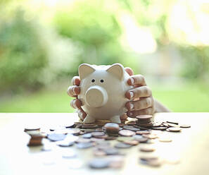 Boy holding piggy bank around coins on table - AJOF01363