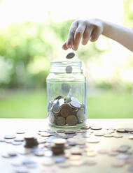 Boy putting coins in glass jar - AJOF01364