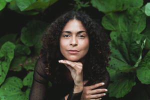 Beautiful woman with hand on chin amidst leaves - FMOF01375