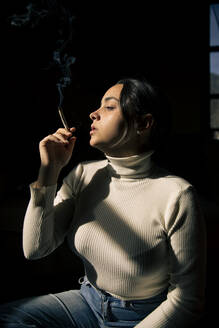 Junge Frau raucht Zigarette im Sonnenlicht zu Hause - ACPF01223