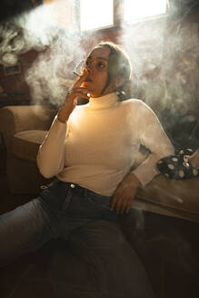 Nachdenkliche Frau schaut weg, während sie zu Hause eine Zigarette raucht - ACPF01225