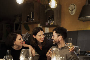 Weibliche Freunde im Gespräch mit lächelndem reifem Mann bei einem Drink zu Hause - MJRF00419