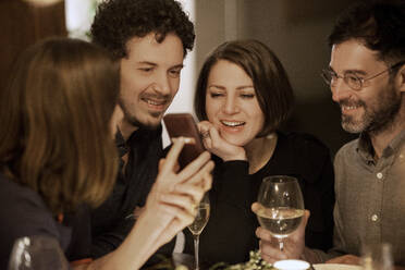 Reife Frau zeigt Handy an männliche und weibliche Freunde während einer Feier zu Hause - MJRF00427