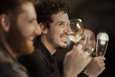 Lächelnde männliche und weibliche Freunde beim Weintrinken zu Hause - MJRF00430
