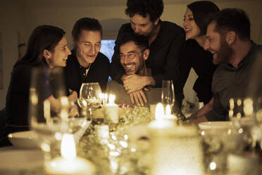 Lächelnde männliche und weibliche Freunde bei einer Geburtstagsfeier zu Hause - MJRF00460