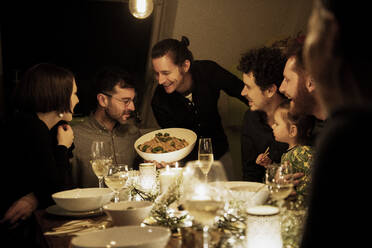 Smiling men and women looking at pasta held by mature man in kitchen - MJRF00469