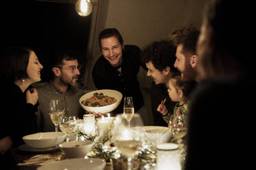 Smiling man holding bowl of pasta at dining table - MJRF00472