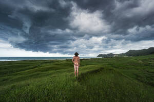 Neuseeland, Nordinsel, Rückansicht eines nackten Mannes mit Blick auf eine Gewitterwolke über blauem Meer - WVF02019