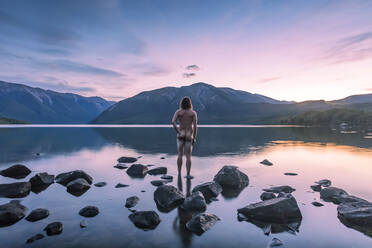 New Zealand, Tasman, Rear view of naked man looking at Lake Rototi at sunset - WVF02022