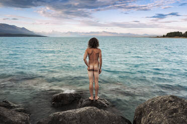 New Zealand, Canterbury, Rear view of naked man looking at Lake Pukaki at sunset - WVF02031