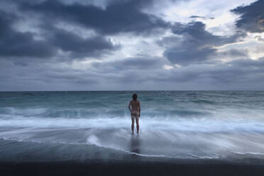Neuseeland, Canterbury, Rückansicht eines nackten Mannes, der unter Gewitterwolken im Meer steht - WVF02034