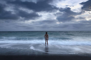 New Zealand, Canterbury, Rear view of naked man standing in sea under storm clouds - WVF02034