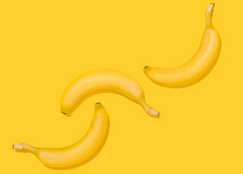 Studioaufnahme von drei liegenden Bananen vor gelbem Hintergrund - FLMF00410