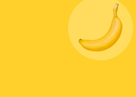 Studio shot of single banana lying against yellow background - FLMF00411