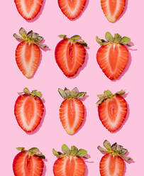Muster von Reihen frischer halbierter Erdbeeren vor rosa Hintergrund - FLMF00424