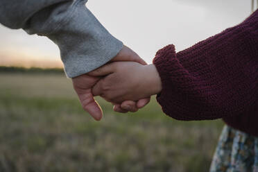 Daughter and father holding hands in field during sunset - EYAF01605