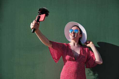 Young woman vlogging while standing by green wall - AGOF00107