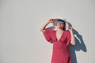 Frau mit Sonnenhut an einer weißen Wand an einem sonnigen Tag - AGOF00108
