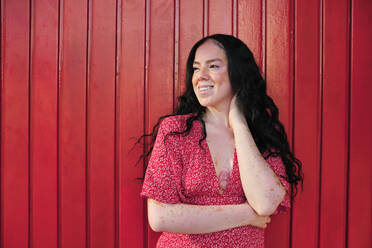 Smiling woman looking away by red wall - AGOF00110