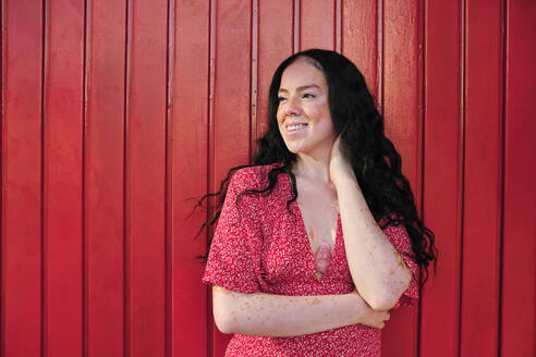 Smiling woman looking away by red wall - AGOF00110