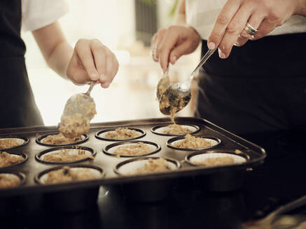 Mutter und Sohn füllen in der Küche ein Muffinblech mit Teig - PWF00310