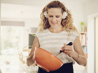 Woman listening music on headphones while mixing ingredient in bowl - PWF00313