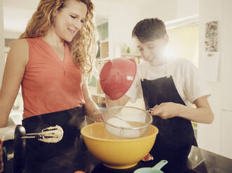 Son sifitng flour with mother while preparing food in kitchen - PWF00317