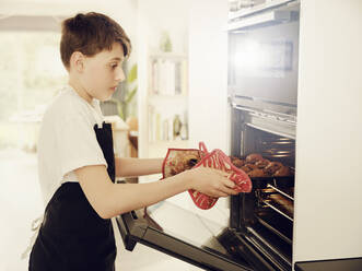 Junge nimmt Muffinblech aus dem Ofen in der Küche zu Hause - PWF00321