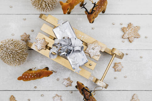 Christmas present on toy sledge surrounded by toy deer with home made cookies against white wooden background - GWF07022