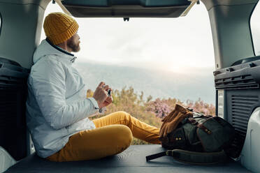 Seitenansicht eines männlichen Campers in warmer Kleidung, der im Van sitzt und die spektakuläre Landschaft der Berge im Urlaub genießt - ADSF24519