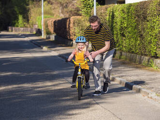 Father teaching cycling to daughter near footpath on road - LAF02711