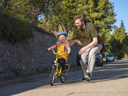 Father supporting daughter while cycling on road - LAF02713