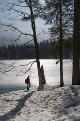 Male backpacker standing by frozen lake while hiking on snow during vacations - MAUF03750