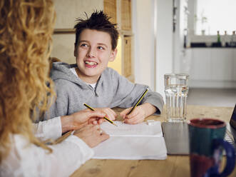 Son smiling while studying by mother at home - PWF00337