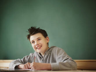 Lächelnder Junge, der beim Lernen zu Hause wegschaut - PWF00345